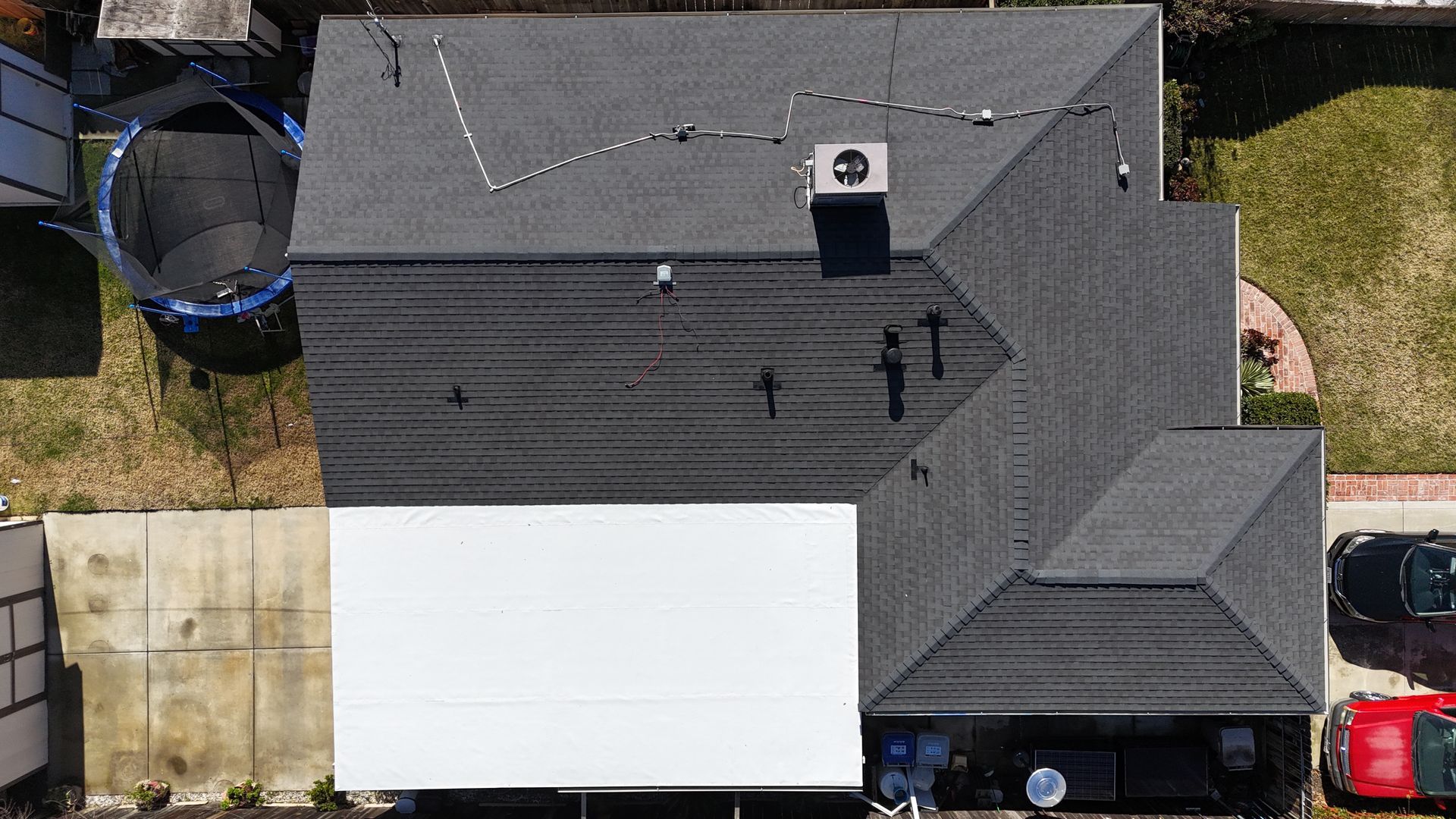 Aerial view of a house with a dark roof, white patio cover, driveway, and parked vehicles.