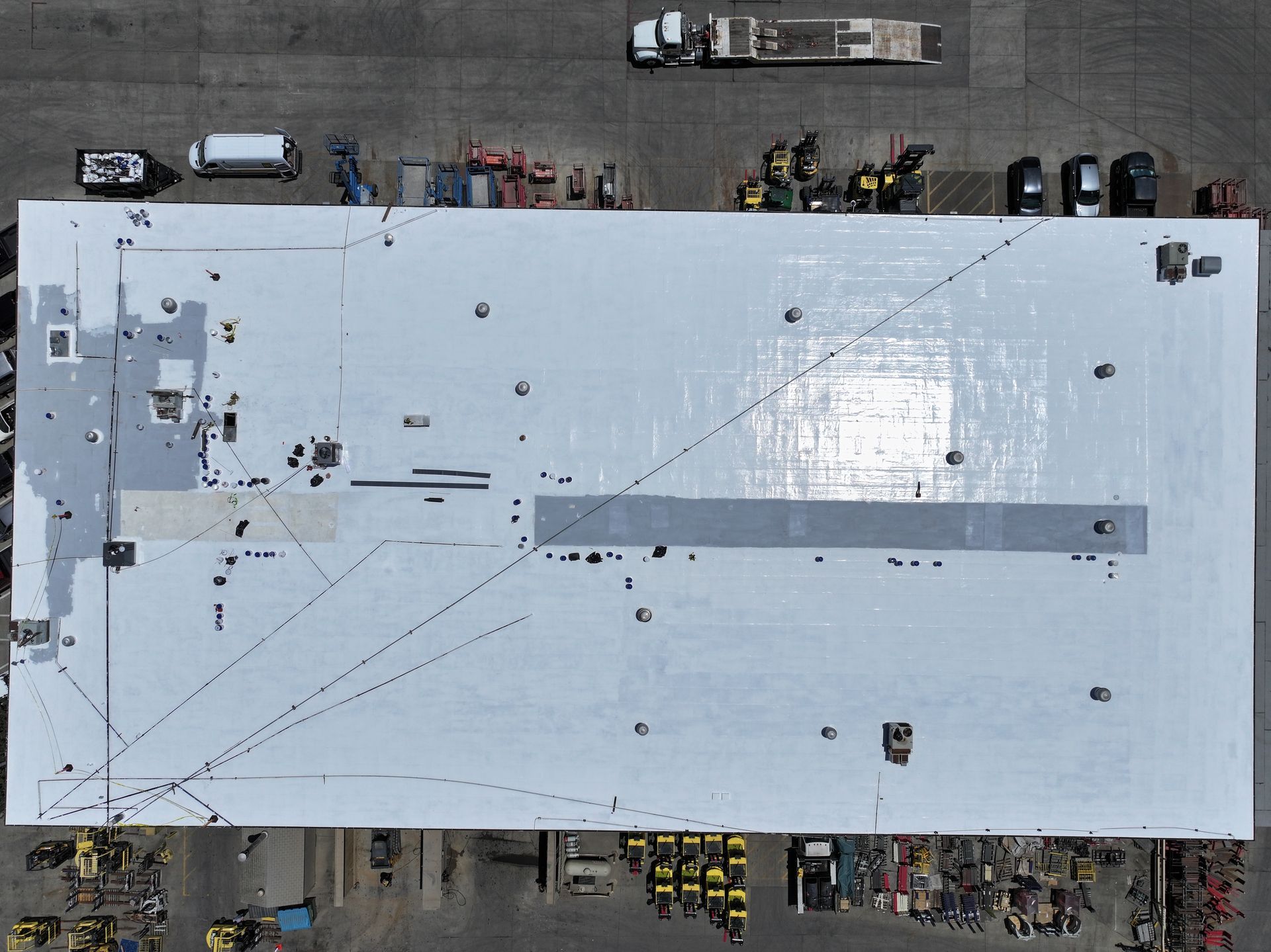 Aerial view of a large white rooftop with workers and vehicles around it.