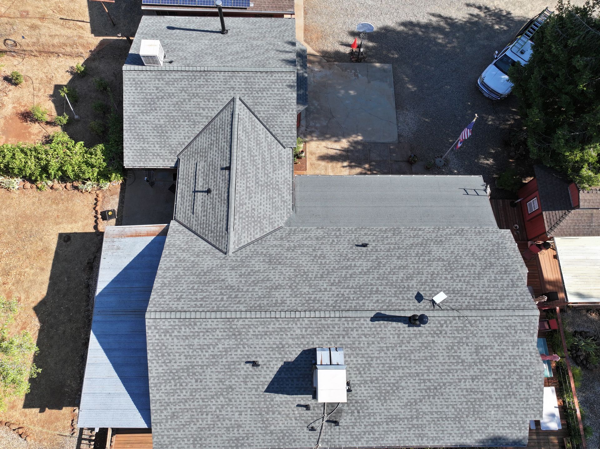 Aerial view of a house roof with gray shingles, skylights, and a driveway beside it.
