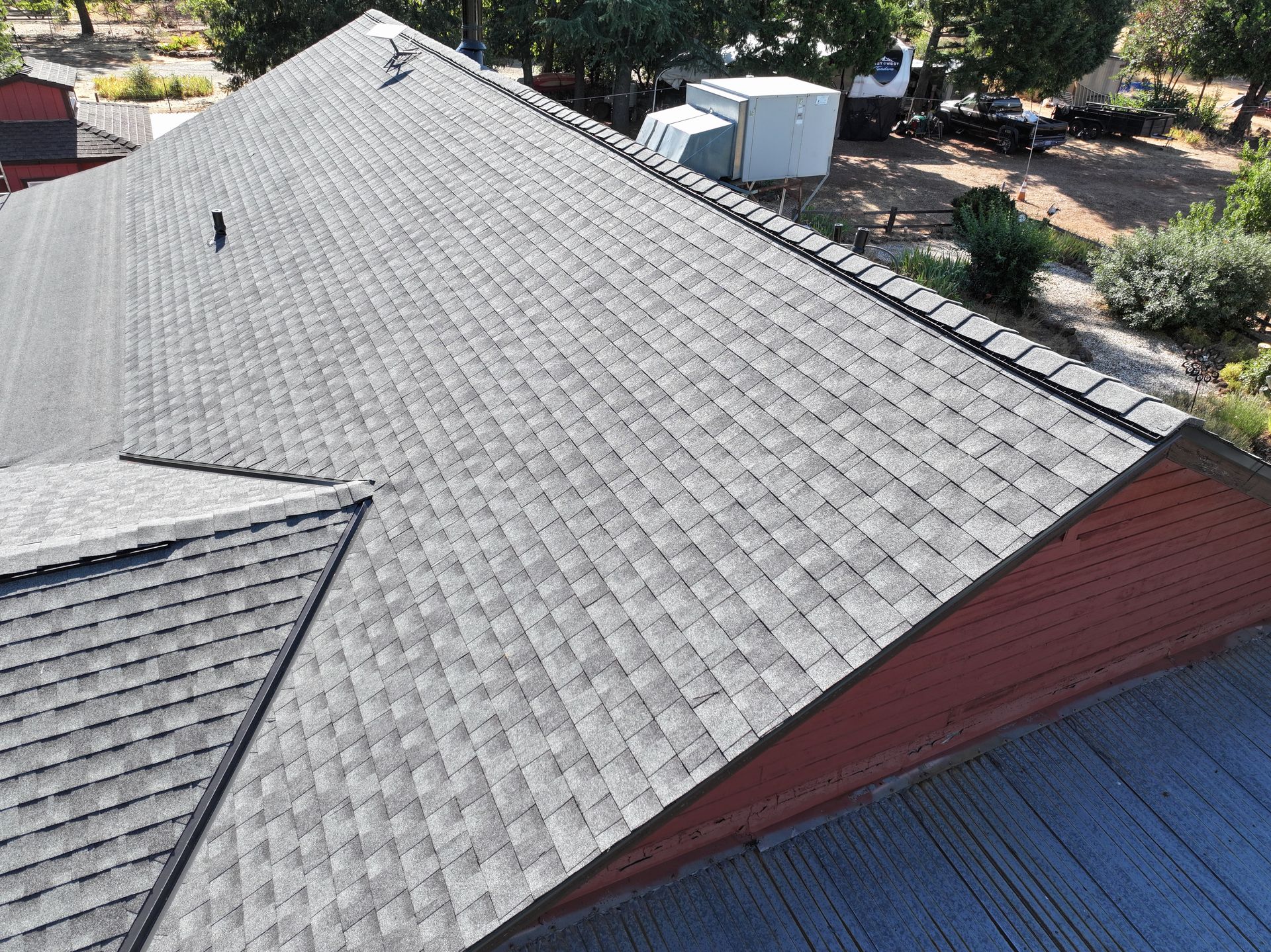 Aerial view of a gray shingled roof with vents and trees in the background