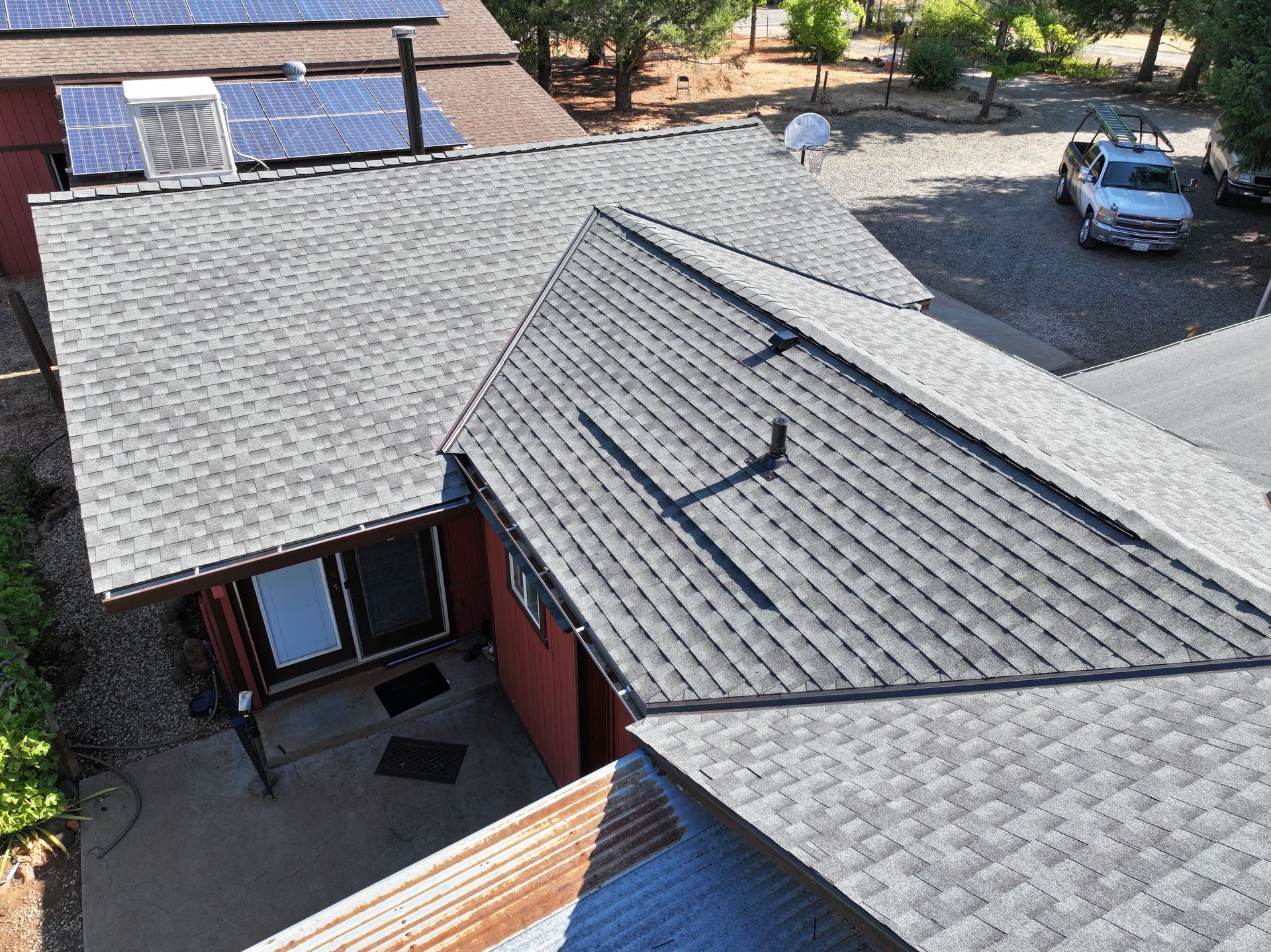 Aerial view of a gray shingled roof on a red house with a driveway and parked car nearby.