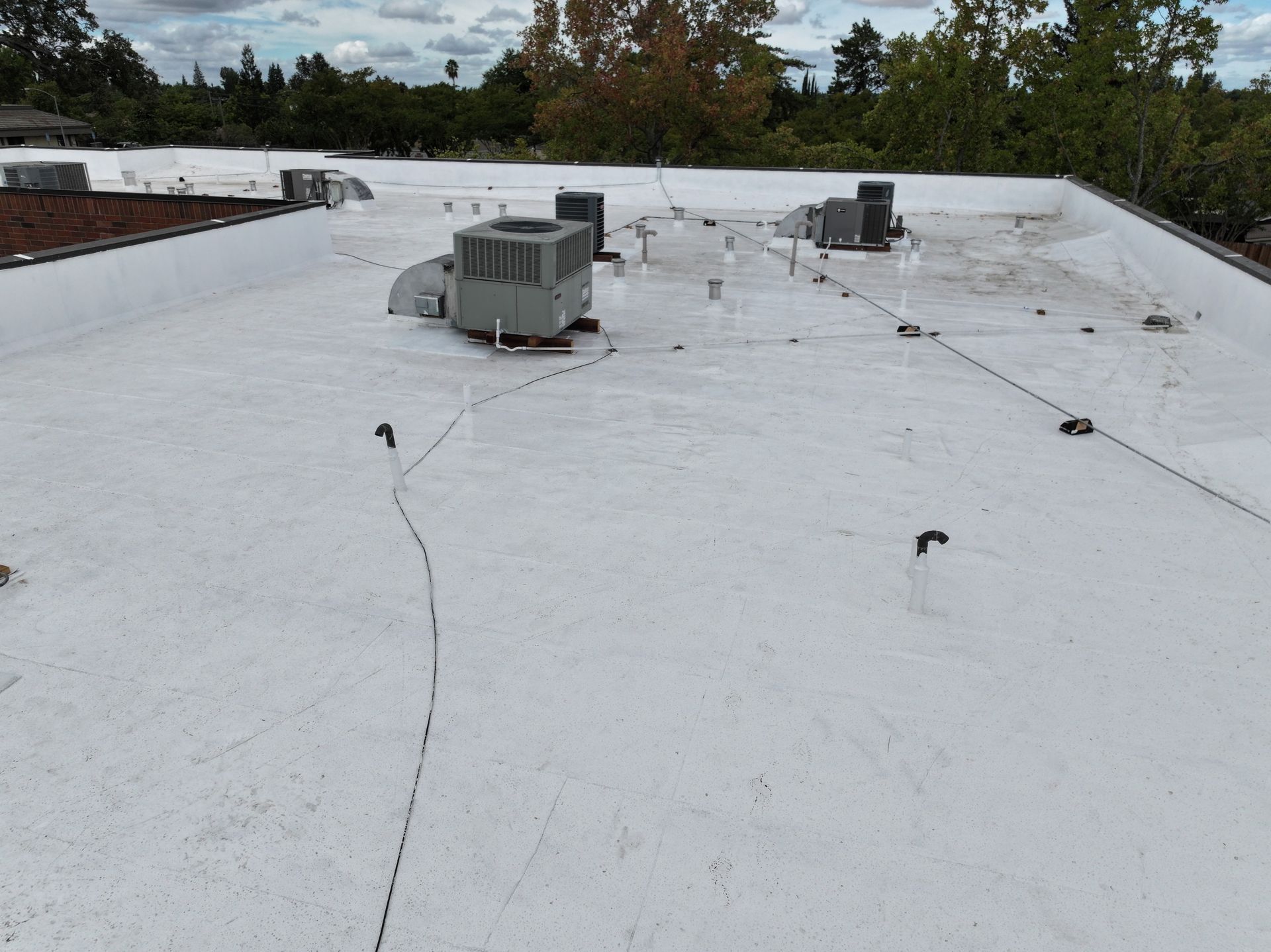 Flat white rooftop with HVAC units and scattered cables under a cloudy sky