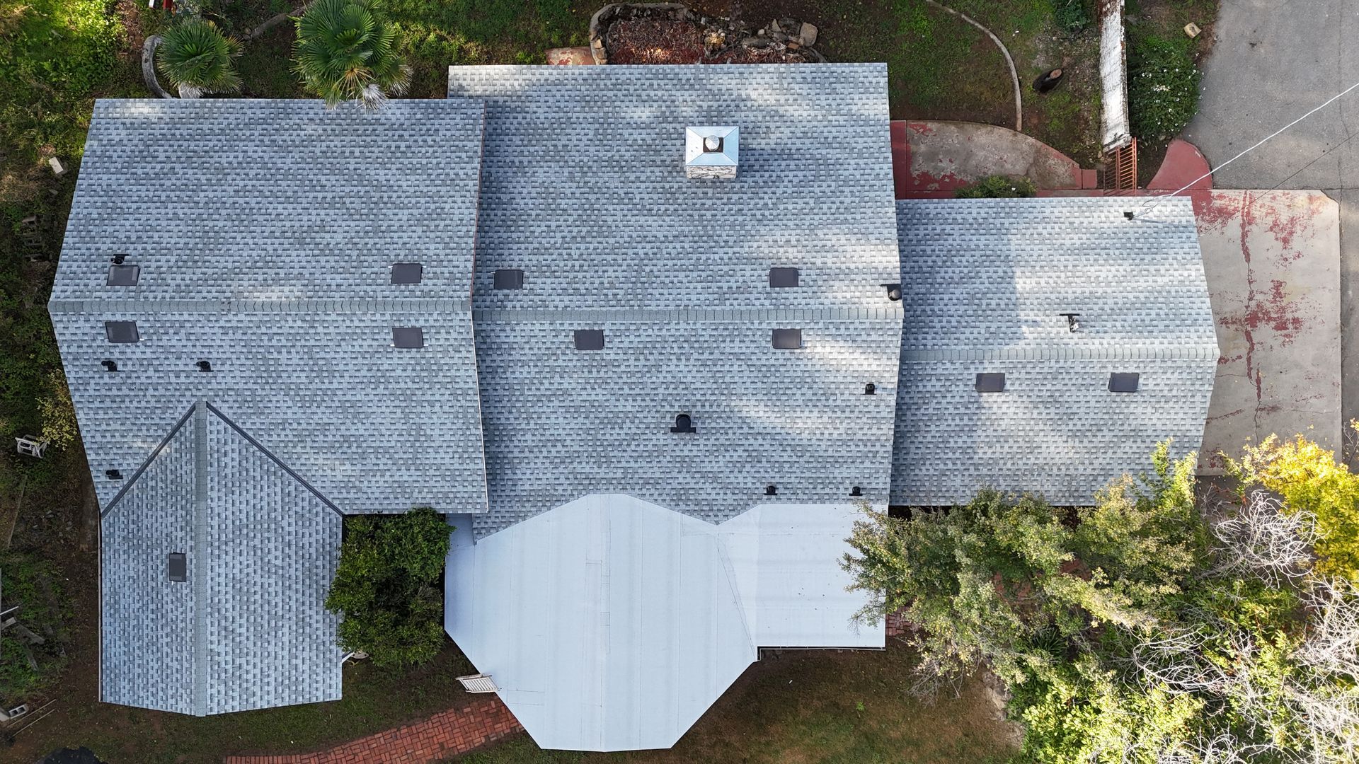 Aerial view of a house with gray roof, dormer windows, and a white covered patio