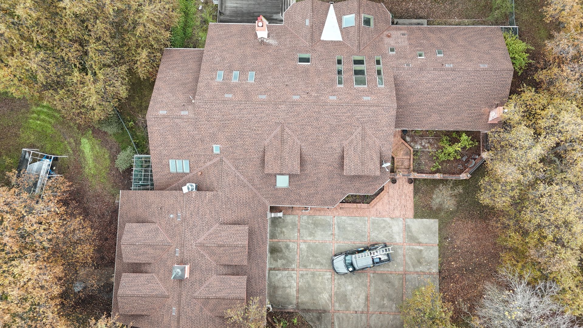 Aerial view of a large brown-roofed house with trees and a car parked in the driveway.