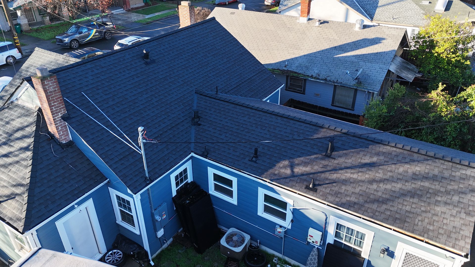 Aerial view of a blue-roofed house and backyard with neighboring homes nearby.