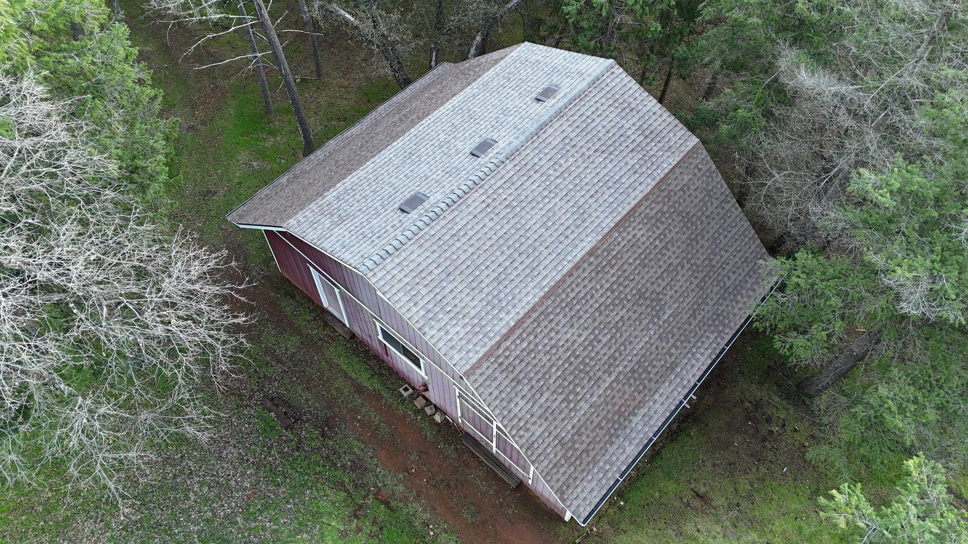 Aerial view of a small red barn with a gray roof surrounded by dense green trees.
