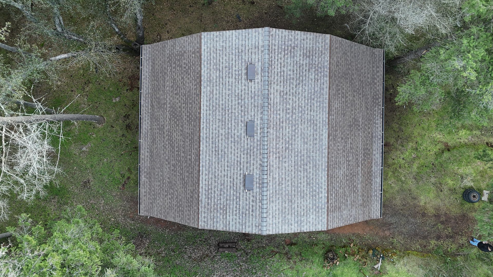 Top-down view of a small gray-roofed building surrounded by dense green trees and brush.