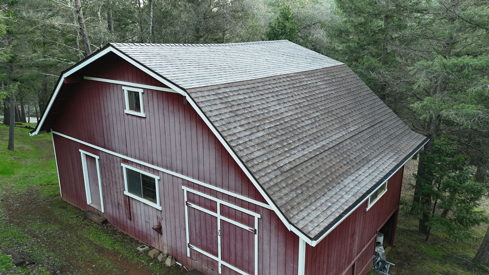 A red barn with a gray roof surrounded by trees, viewed from above.