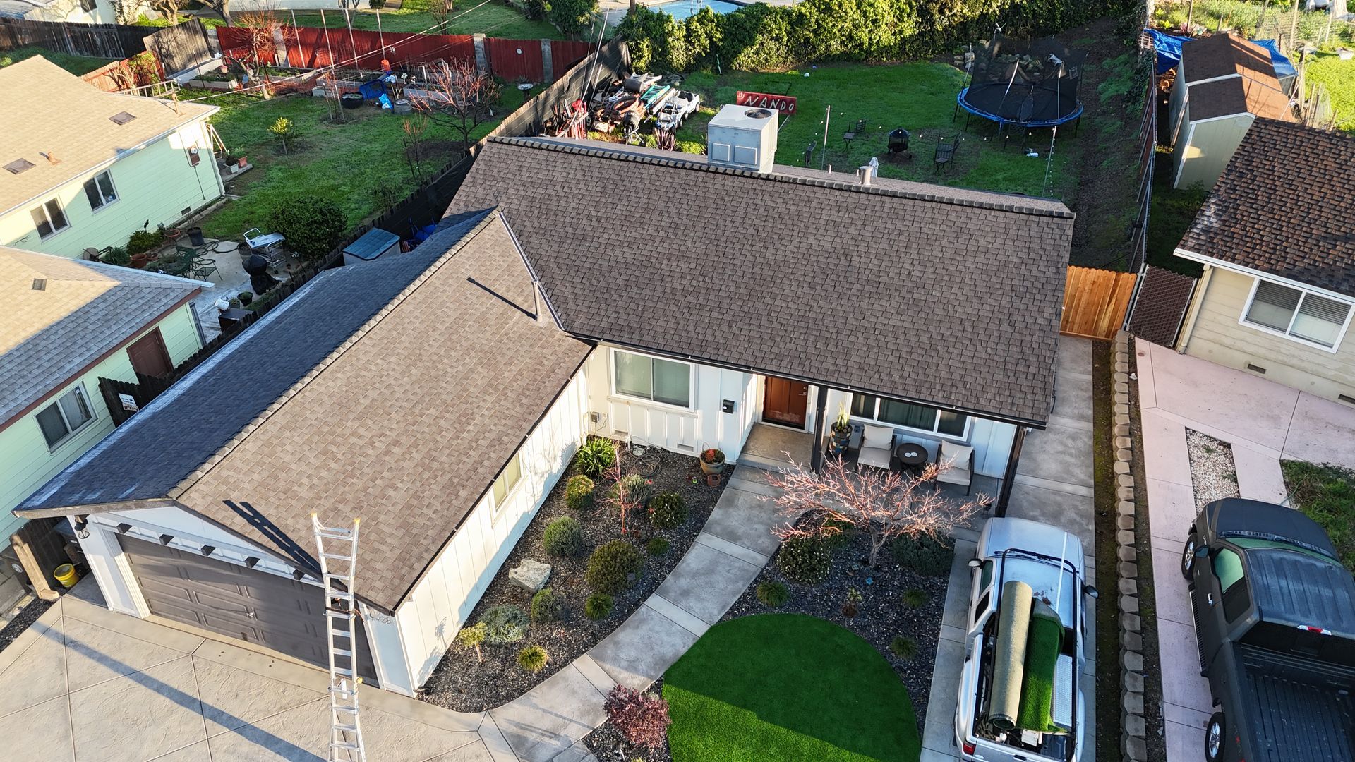 Aerial view of a white house with a dark roof, curved walkway, front lawn, and parked car.