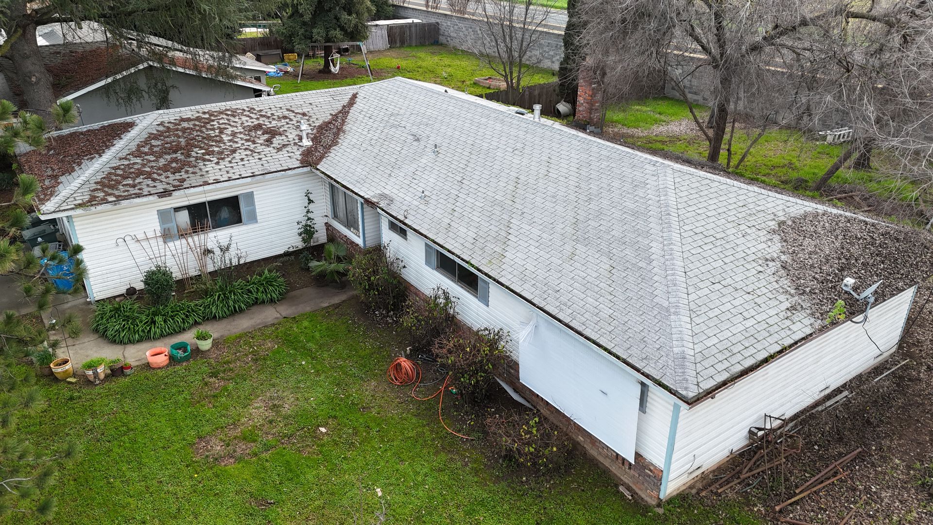 Aerial view of a white house with a gray roof and a small yard, surrounded by trees.