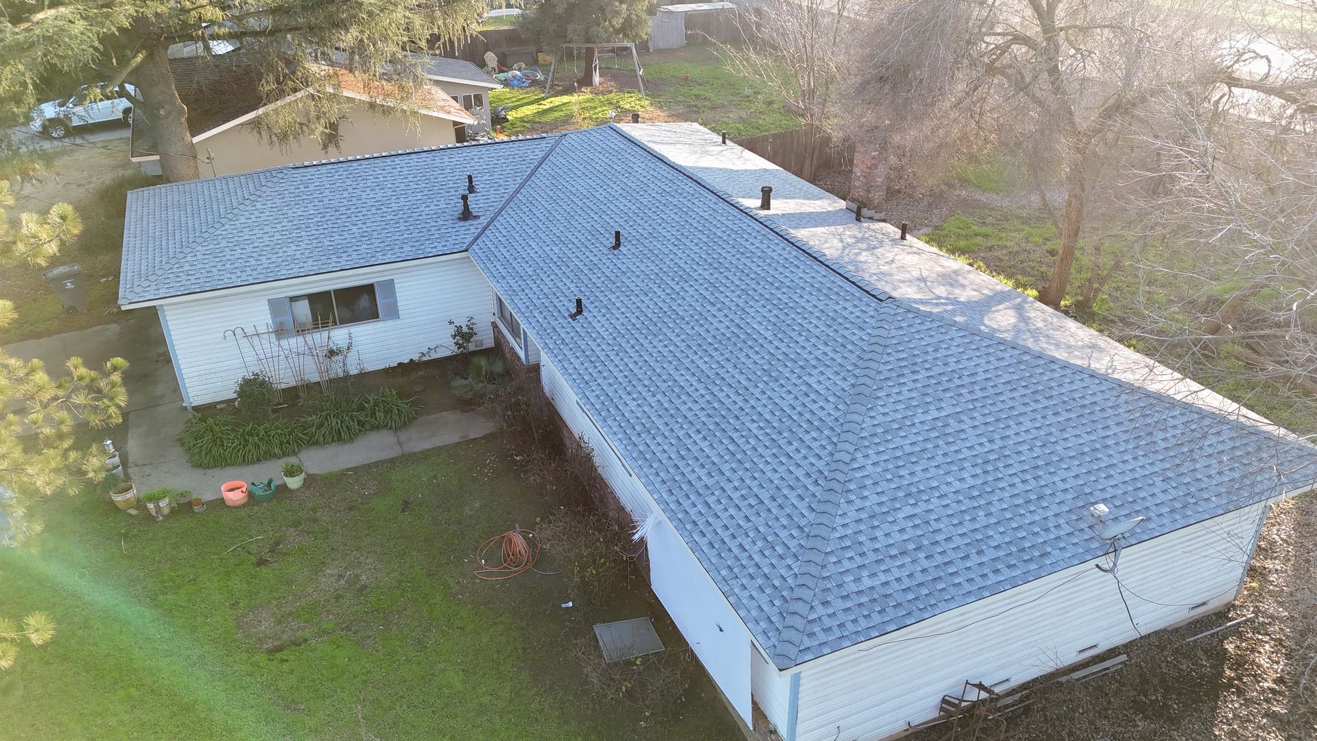 Aerial view of a white house with a blue roof surrounded by trees and a grassy yard