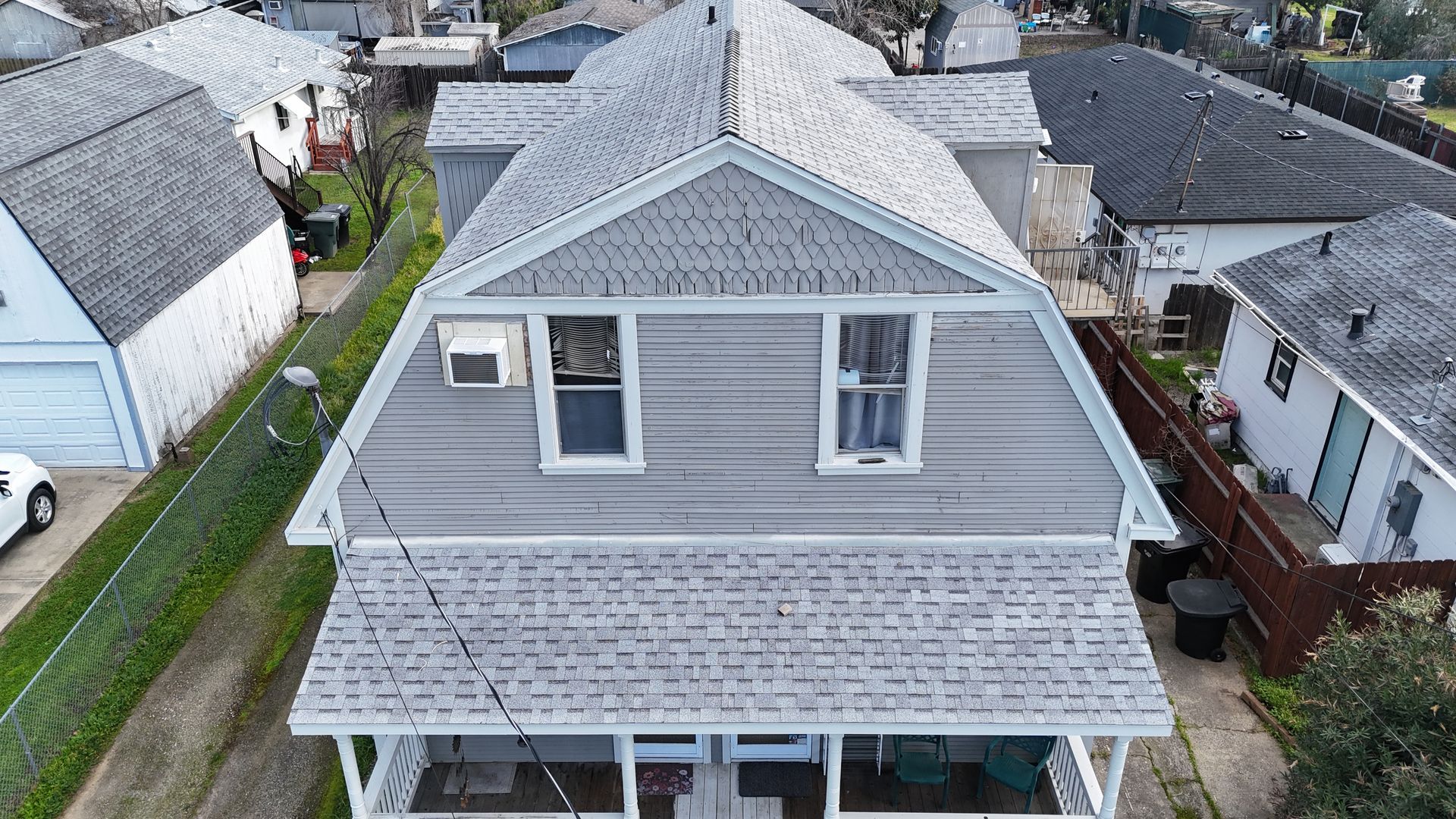 Aerial view of a gray two-story house with a covered porch in a residential neighborhood
