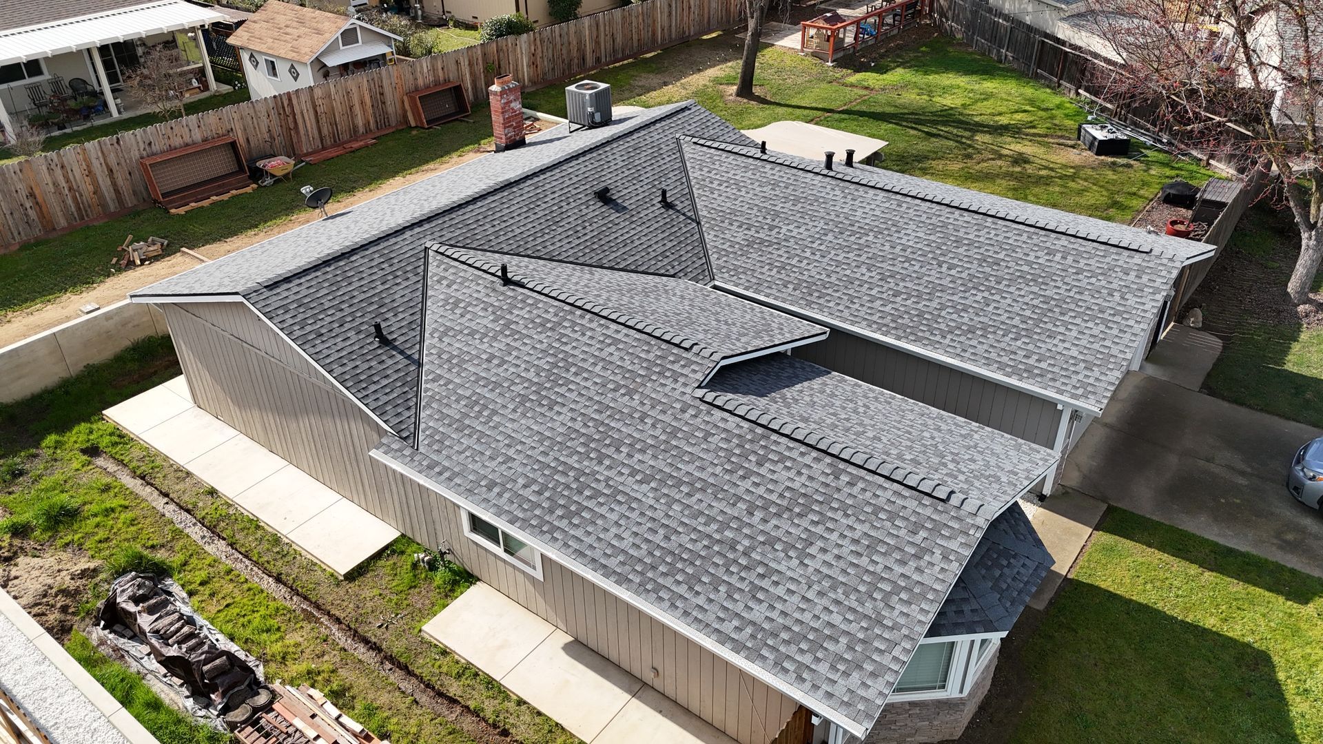 Aerial view of a gray shingled house with a large roof and fenced backyard.
