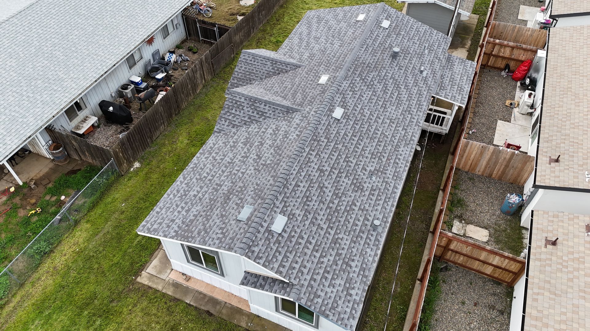 Aerial view of a gray-roofed house with a fenced yard and neighboring homes.