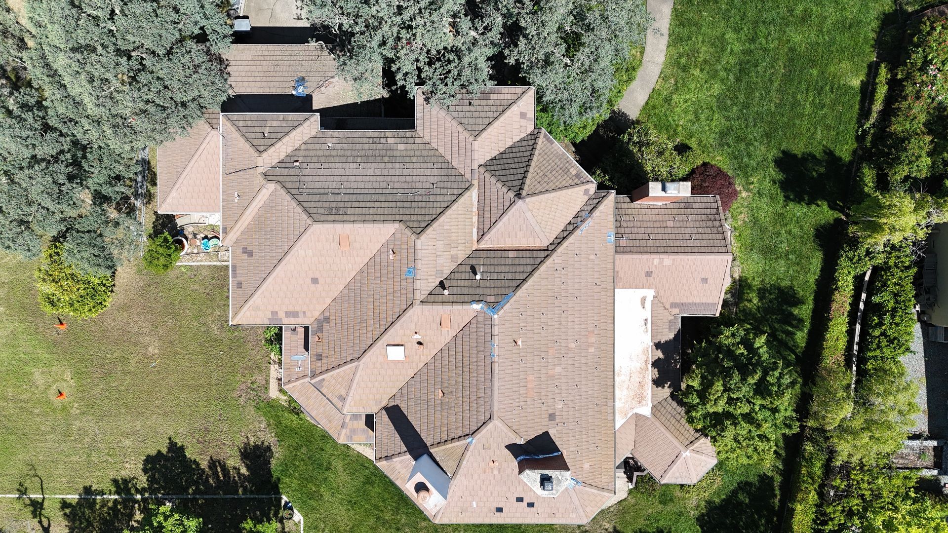 Aerial view of a tan-roofed house surrounded by lawn, trees, and a garden path.