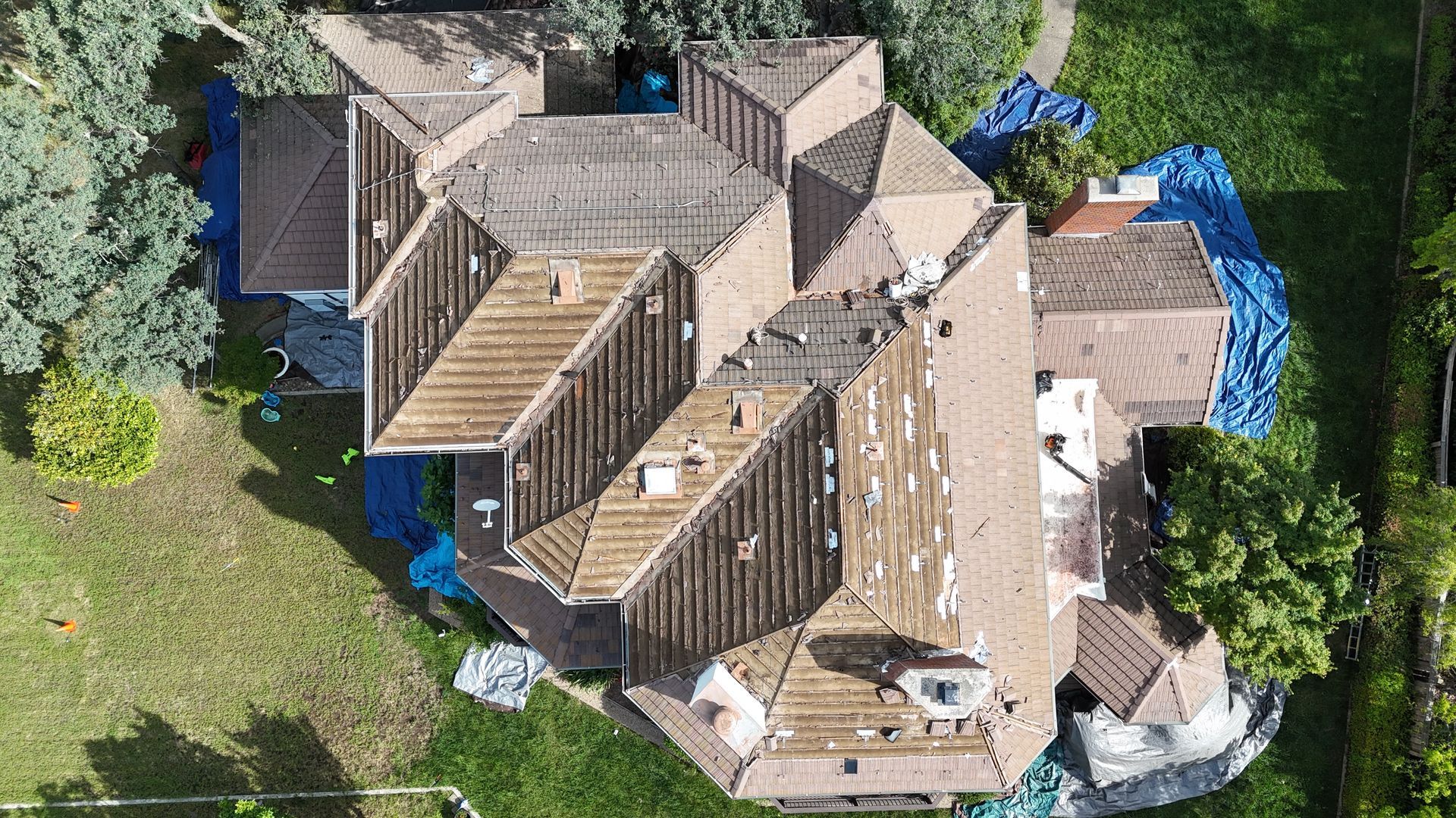 Aerial view of a tan-roofed house surrounded by green trees and a yard.