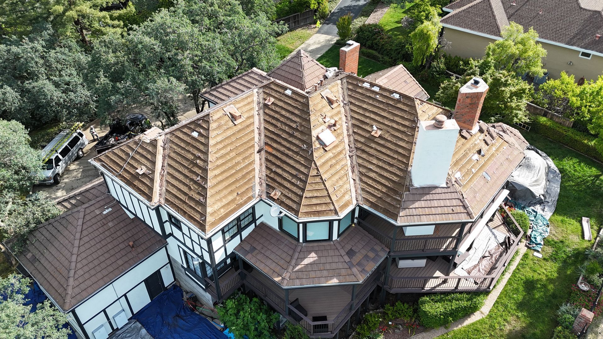 Aerial view of a large tan-roofed house surrounded by green trees and a driveway.