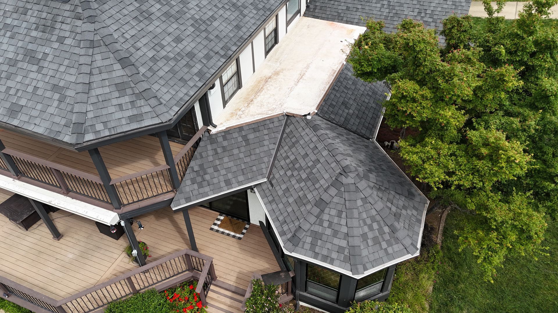 Aerial view of a house with gray roof, porch, and trees around it