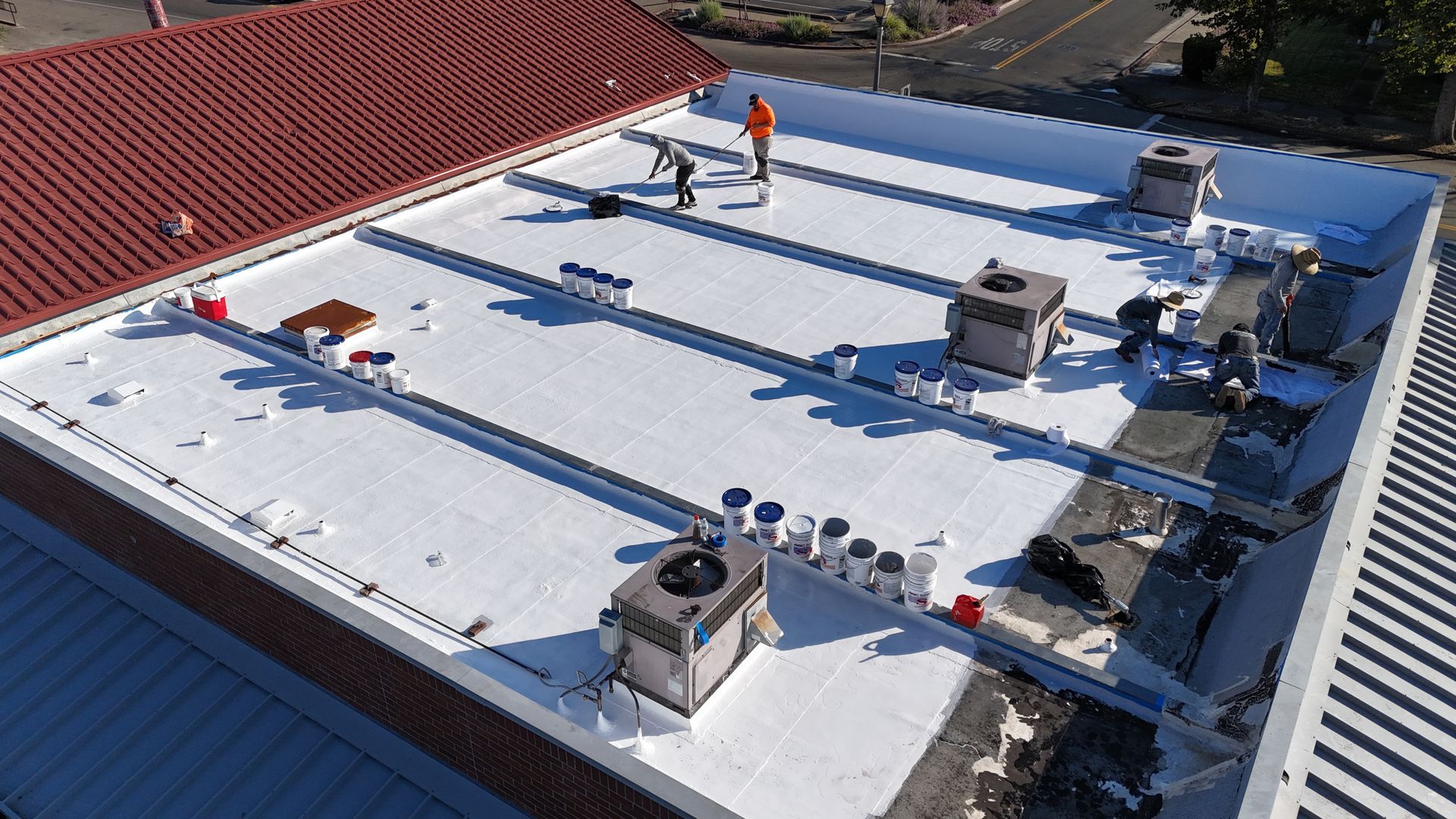Rooftop with white membrane, HVAC units, and workers near the edge under bright sun