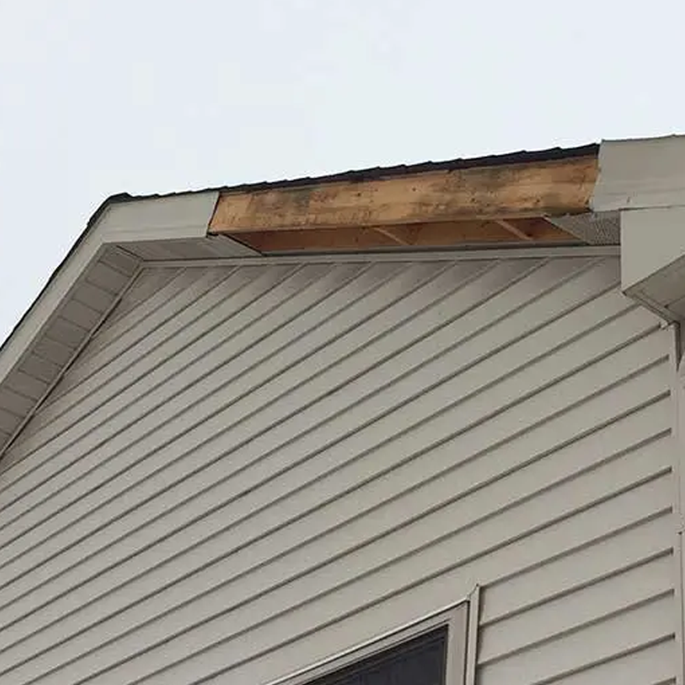 Damaged roof edge above beige siding with exposed wood under the trim