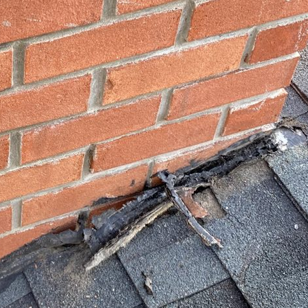 Damaged roof edge with exposed wood under red brick wall and dark shingles