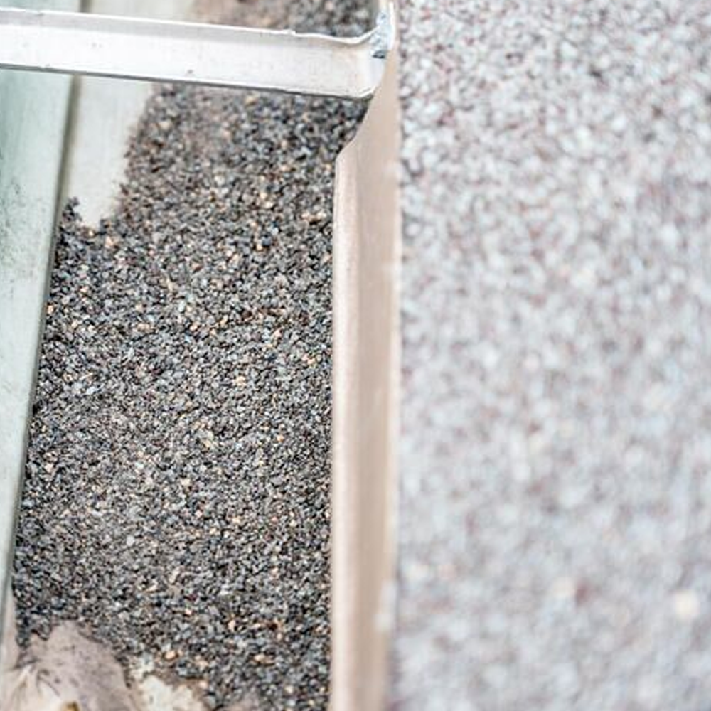 Close-up of gravel being poured from a chute into a narrow channel or tray