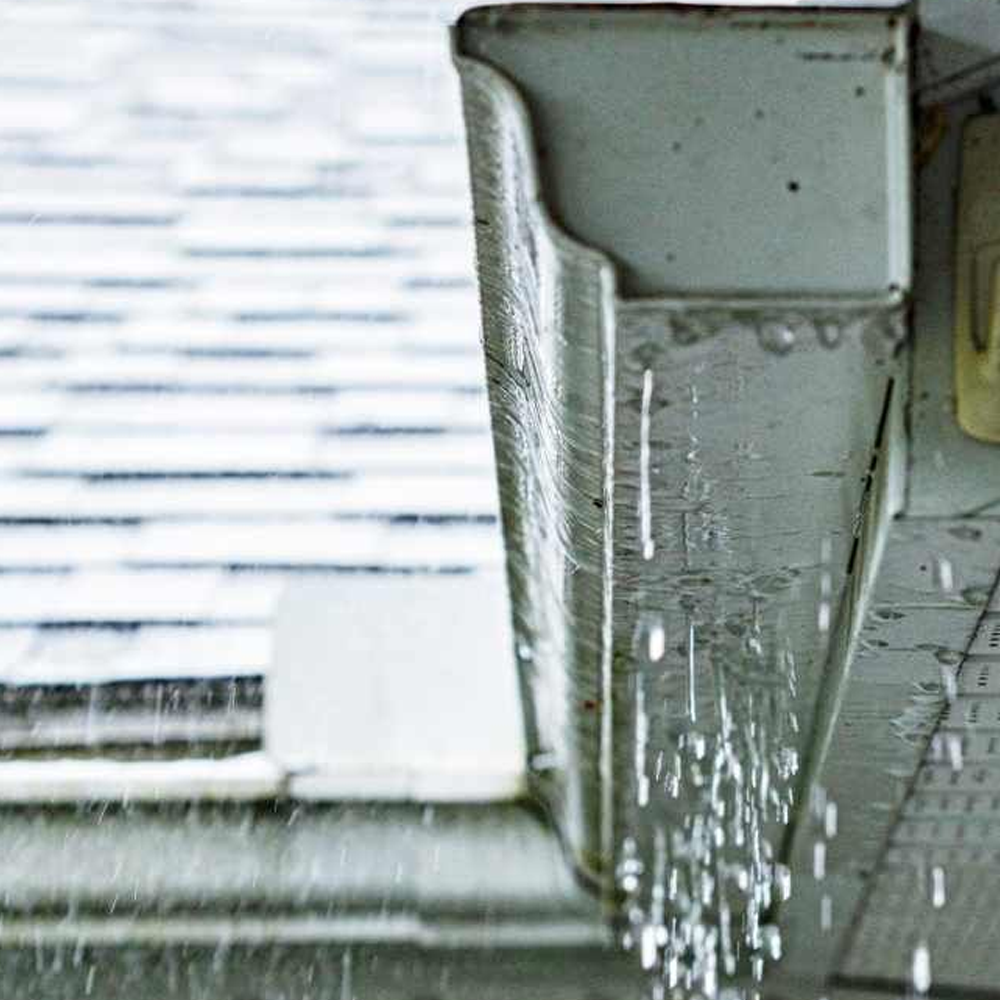 Rainwater dripping from a white roof gutter onto a wet deck