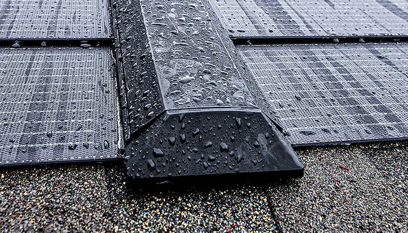 Close-up of a dark metal roof vent on a wet shingled roof with water droplets