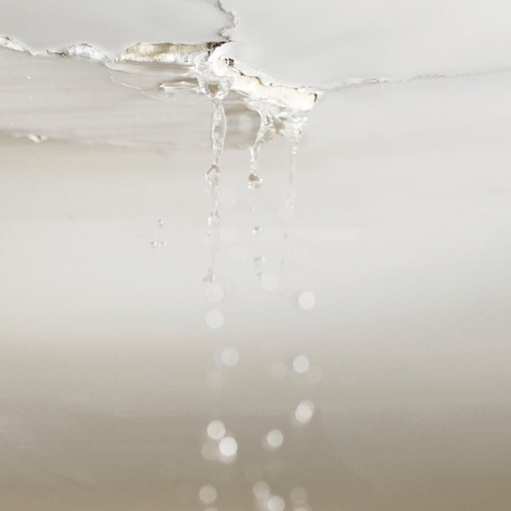 Water leaking through a cracked white ceiling, dripping into the room