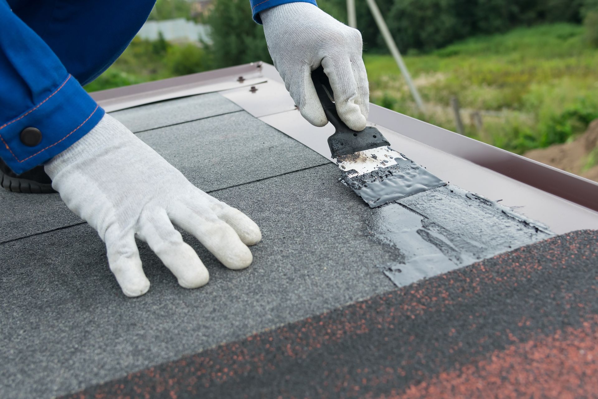 Gloved hands applying roof sealant to a flat rooftop seam with a putty knife