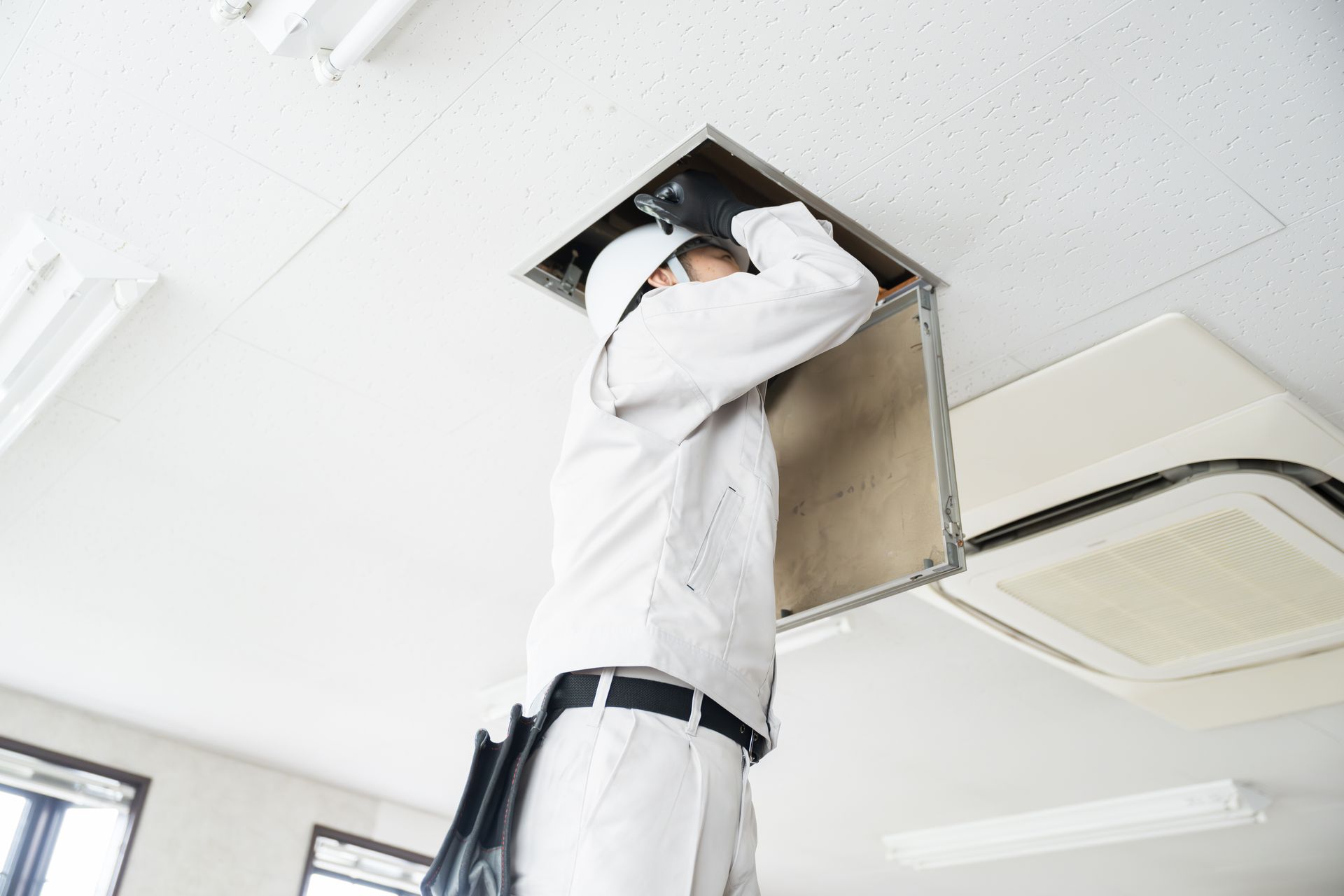 Technician opening a ceiling vent panel in a white office room