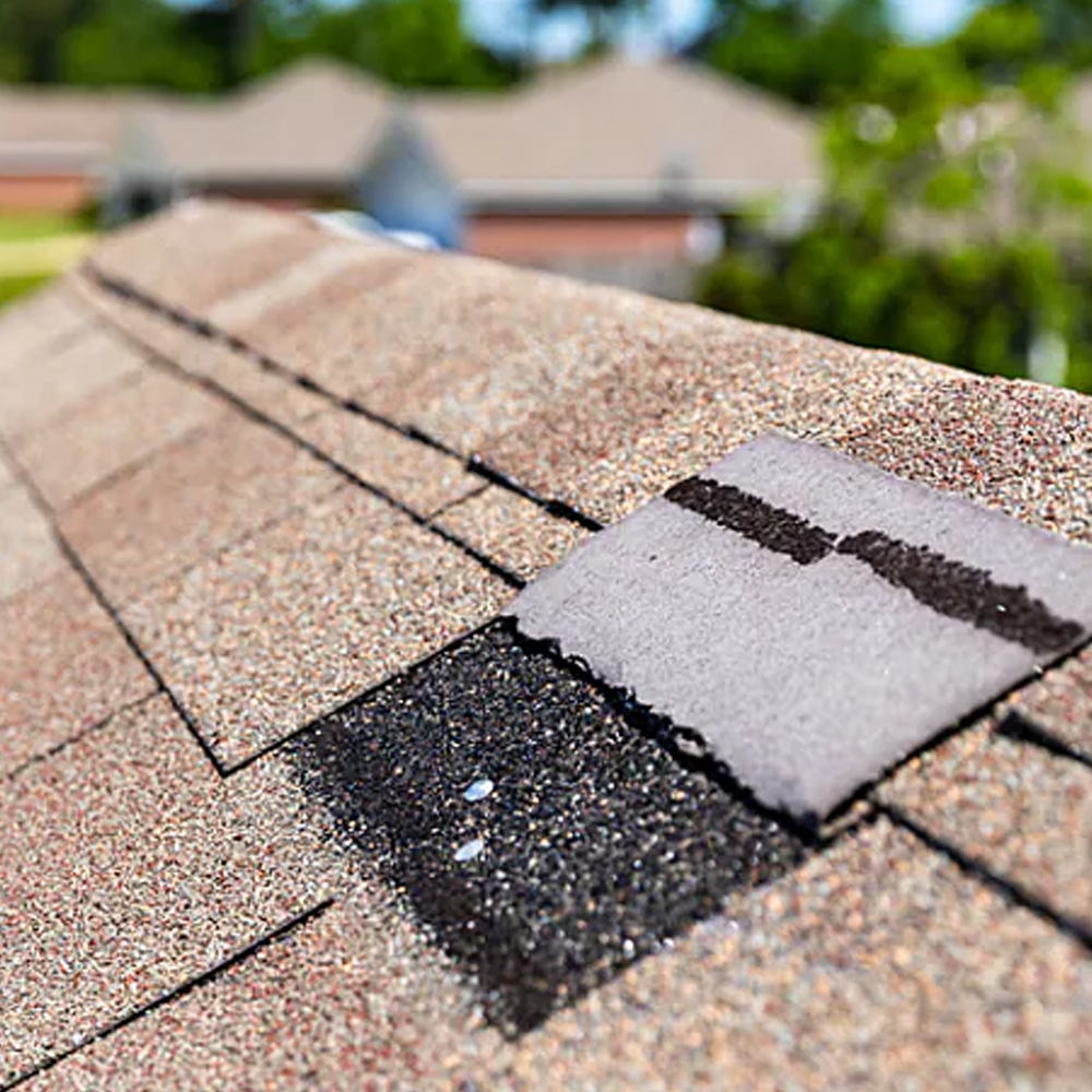 Damaged asphalt roof shingles with a patched, mismatched shingle section