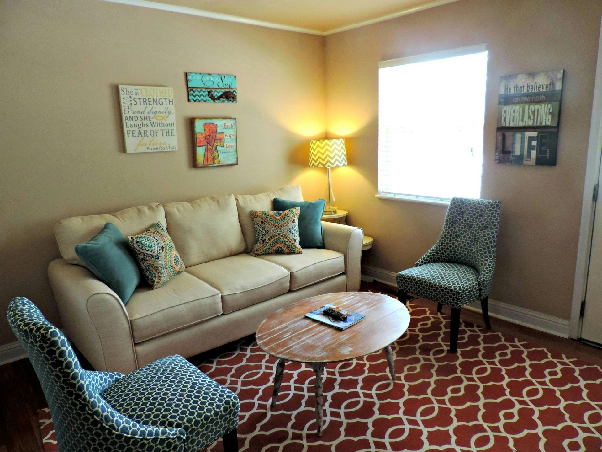 Cozy living room with beige sofa, patterned chairs, red rug, lamp, and wall art by a bright window
