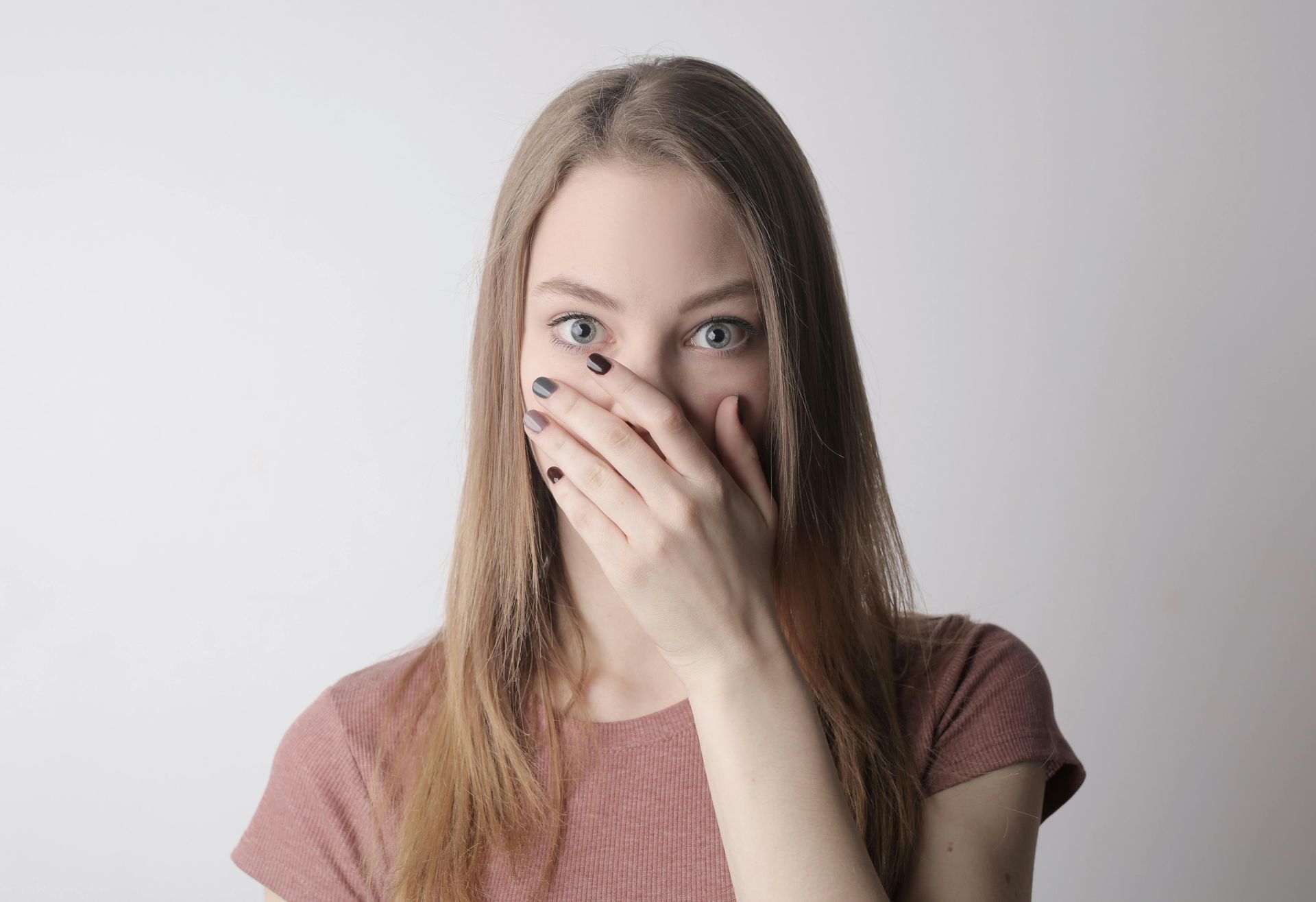 Young person covering their mouth with one hand, looking at the camera against a light background