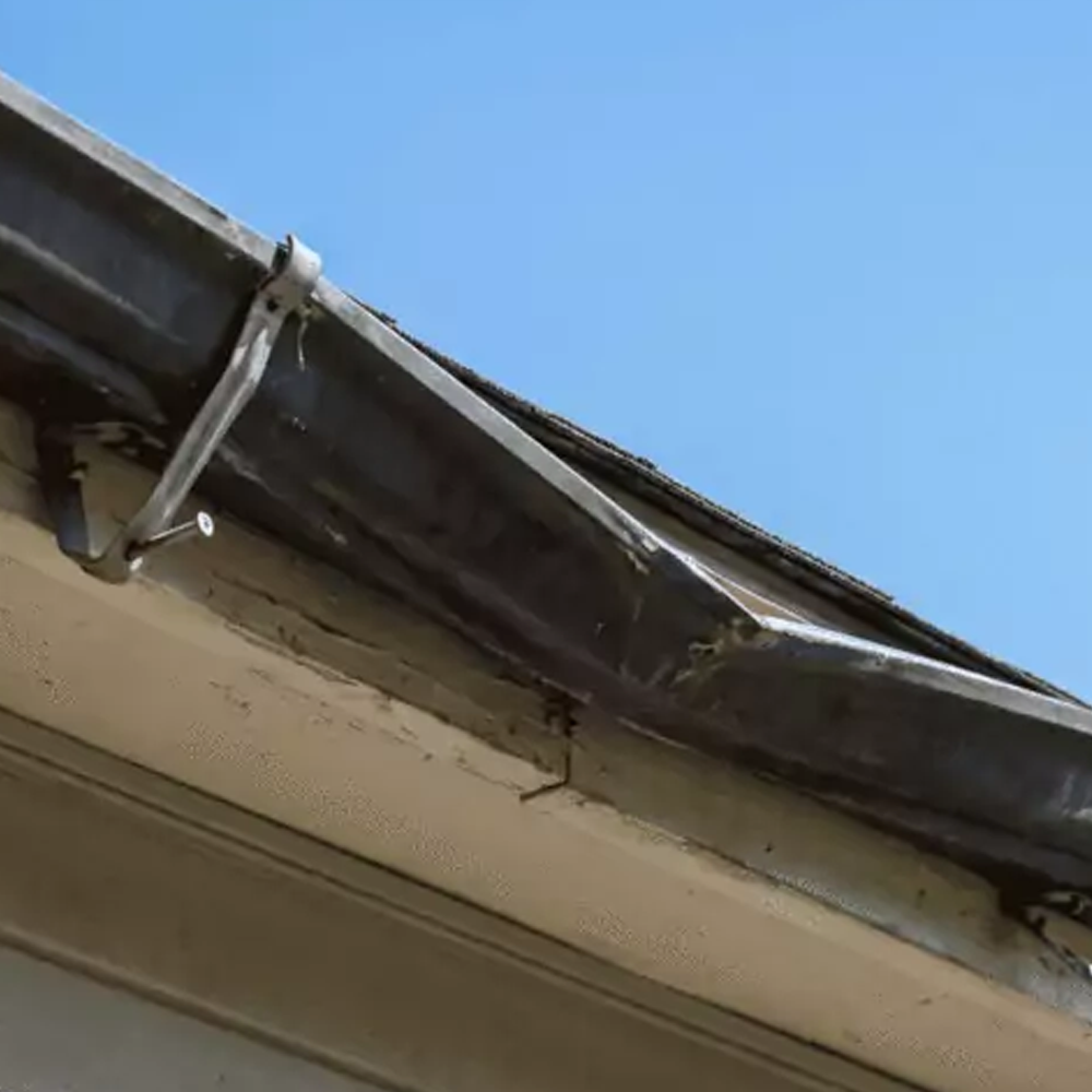 Damaged roof gutter with bent metal bracket against a blue sky