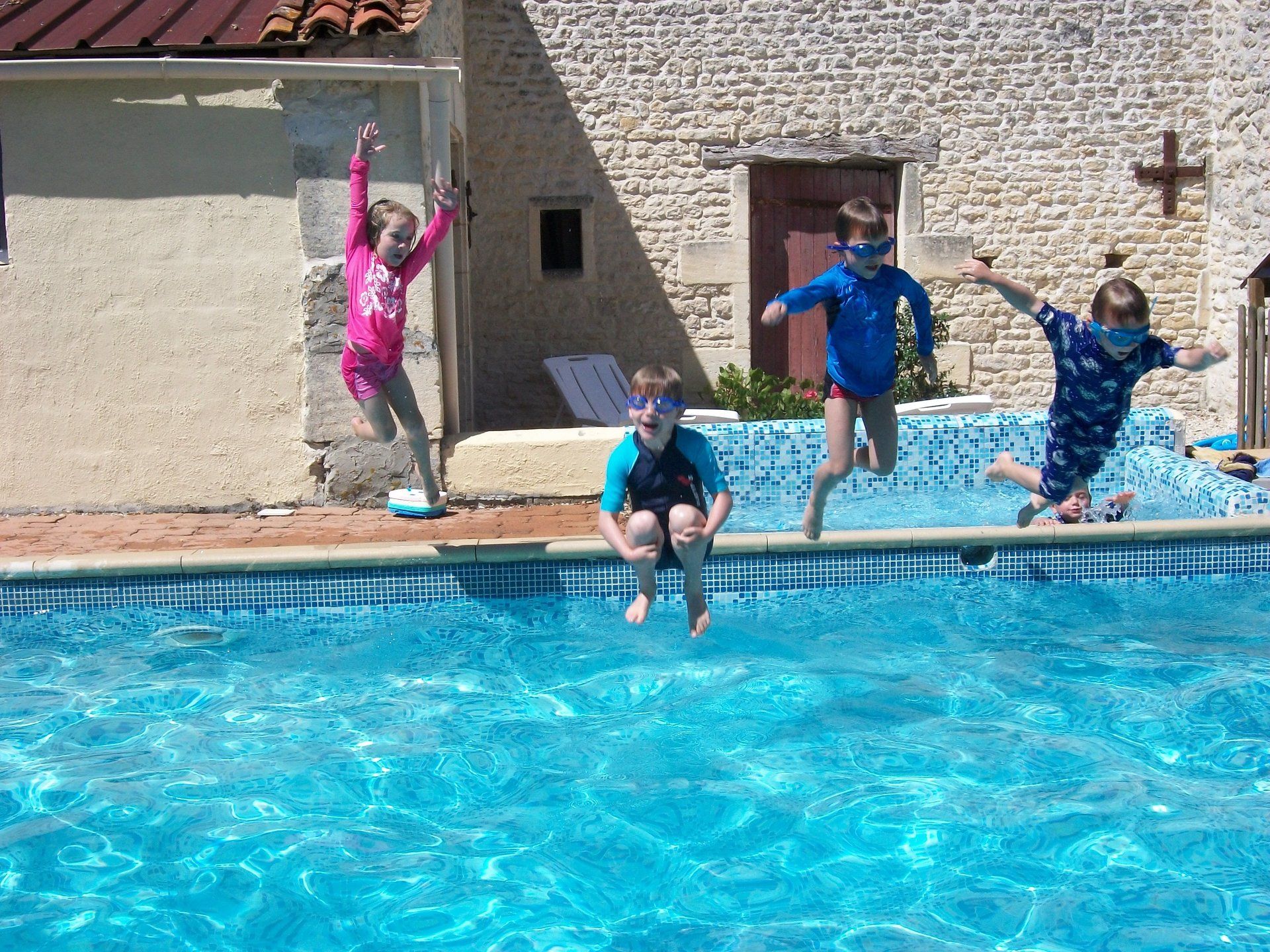 a girl and three boys jumping up high in the air into a swimming pool