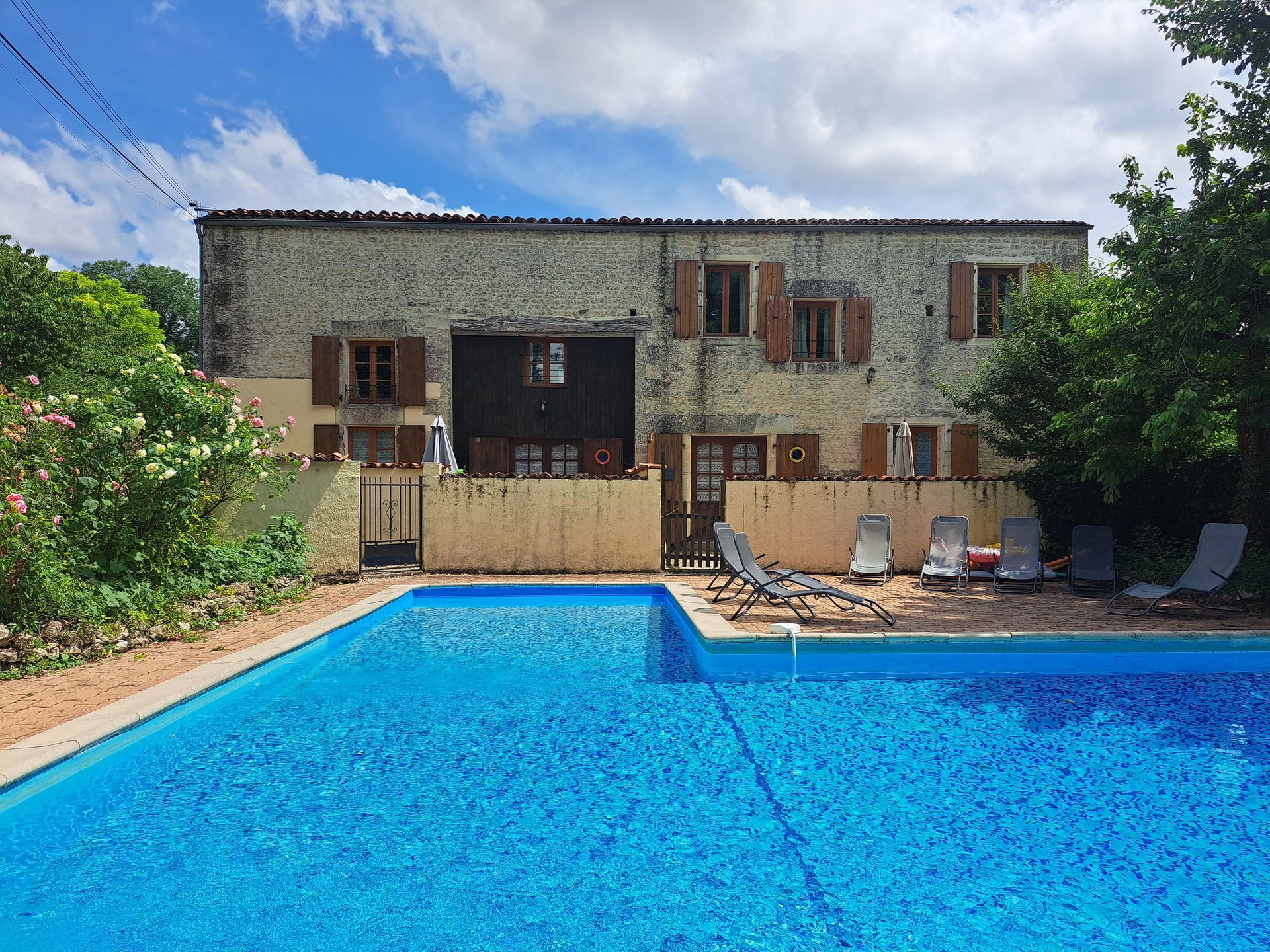 L shaped swimming pool in front of a stone holiday cottage with greay sunbeds