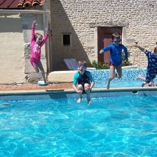 a girl and three boys jumping up high in the air into a swimming pool
