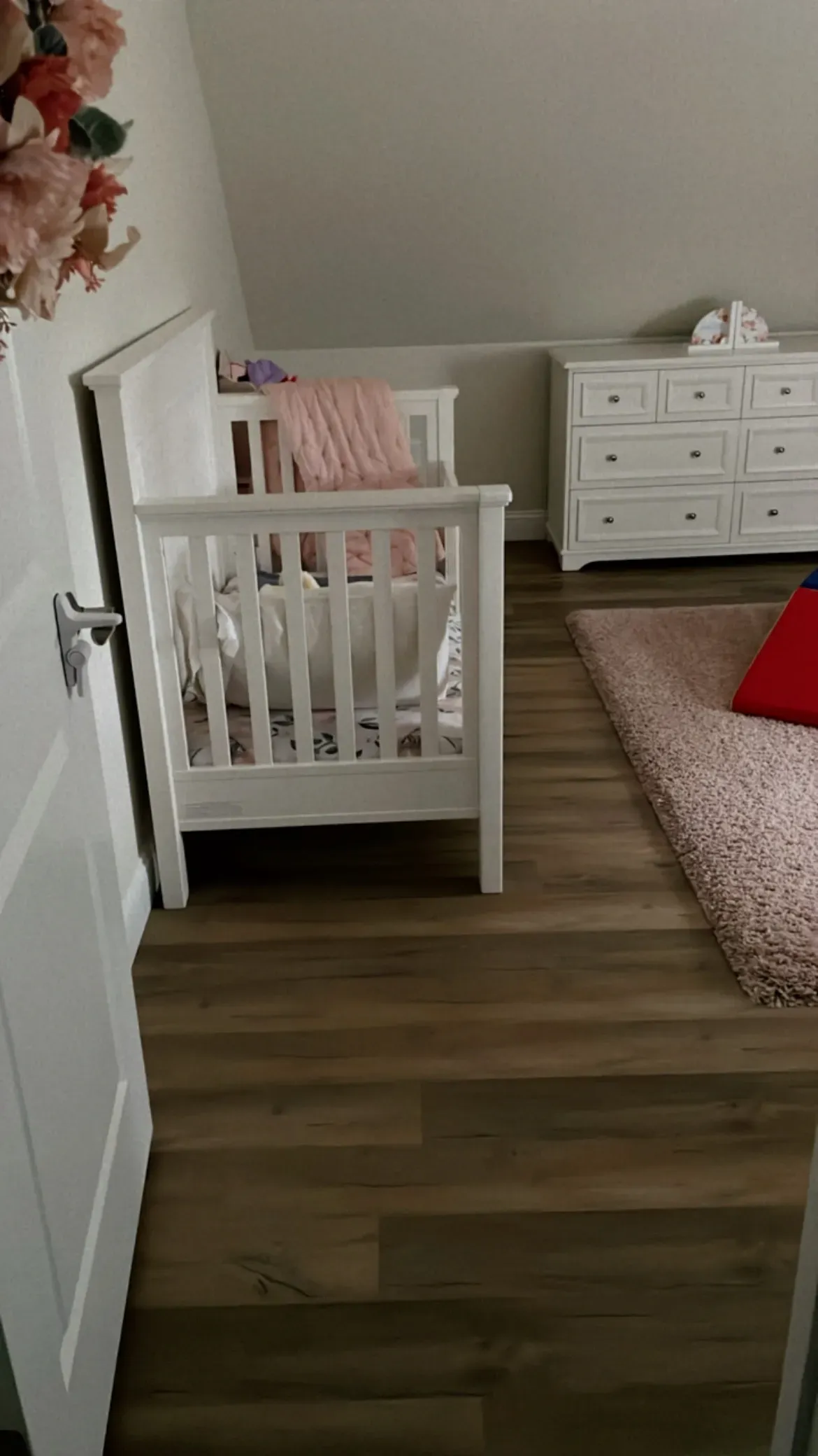 A baby crib is sitting in a room next to a dresser.