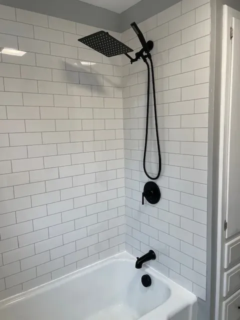 A bathroom with white brick walls and a bathtub with a black shower head.
