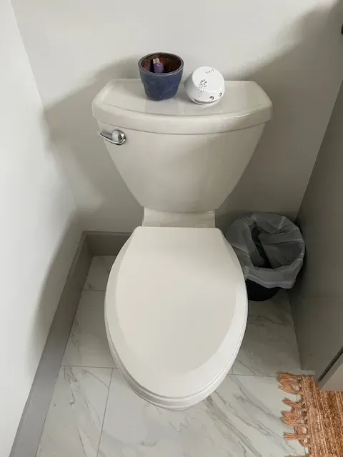A white toilet is sitting in a bathroom next to a trash can.