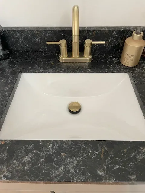 A bathroom sink with a gold faucet and a black counter top.