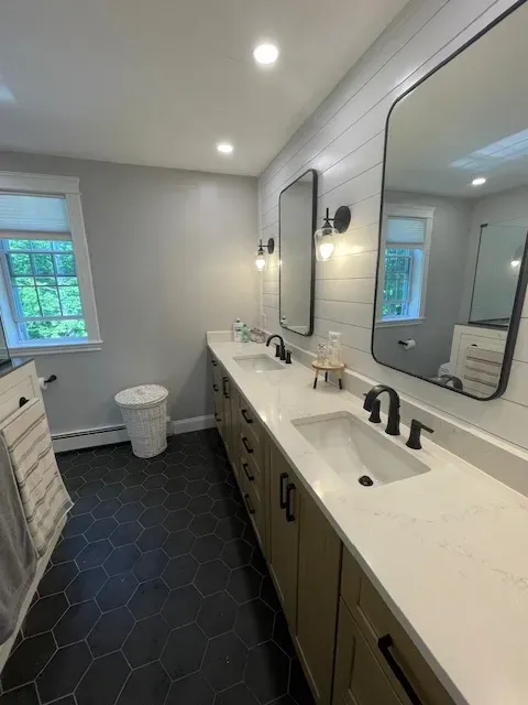 A bathroom with two sinks , two mirrors and a toilet.