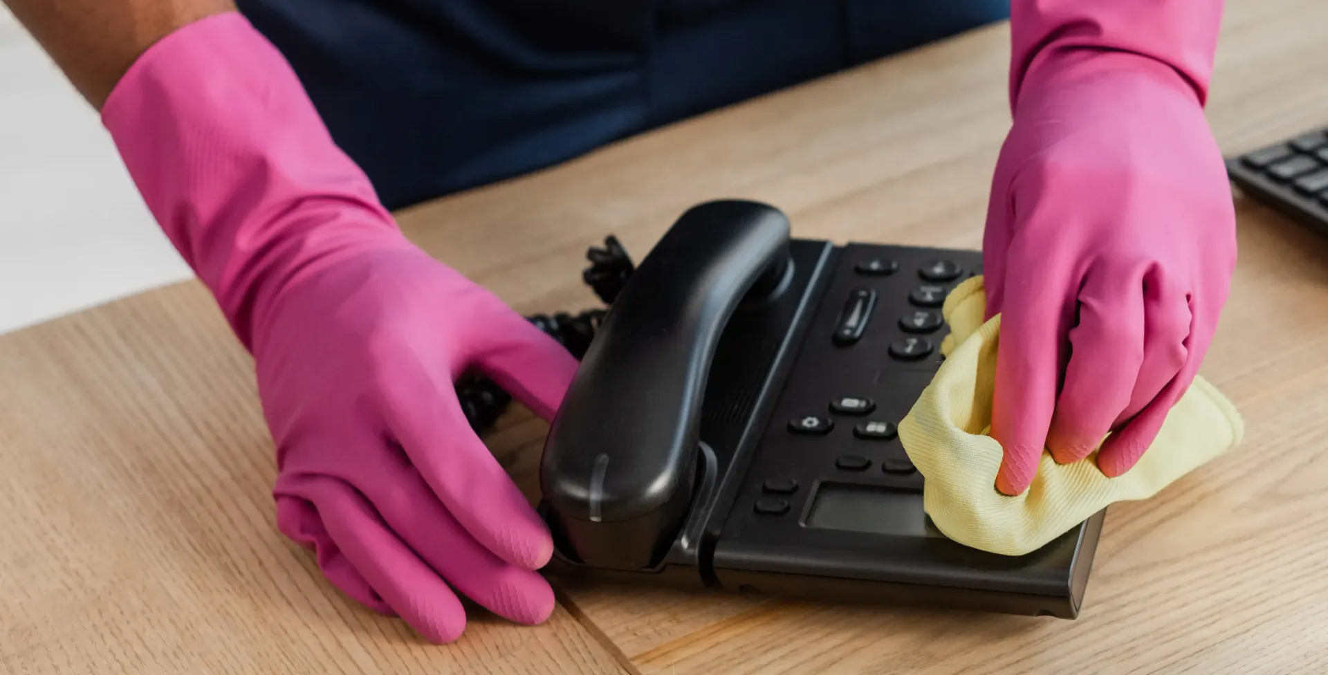 A person wearing pink gloves is cleaning a telephone on a desk.