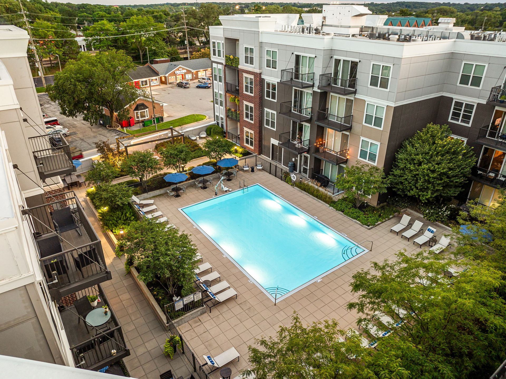 Aerial view of Marq on Main apartment complex with a rectangular pool surrounded by lounge chairs and trees.