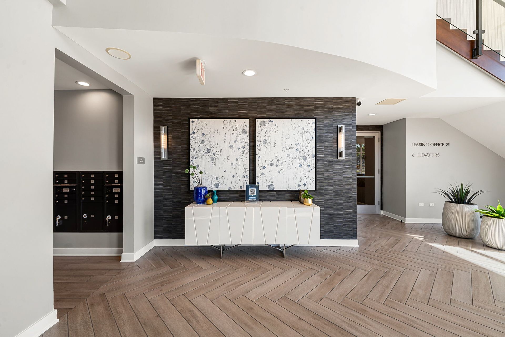 Modern apartment lobby with herringbone floors, artwork, and a dark accent wall.