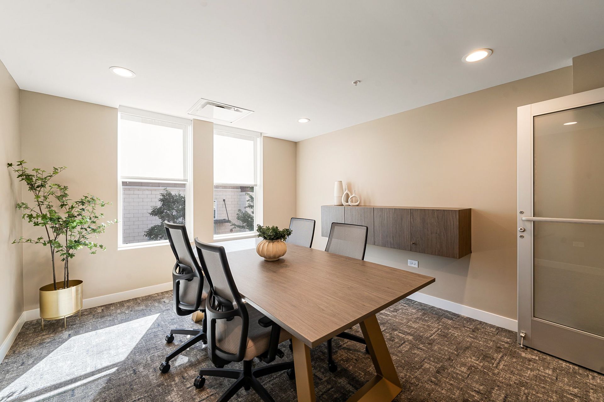 Conference room with a wooden table, chairs, and windows. Beige walls and carpet.