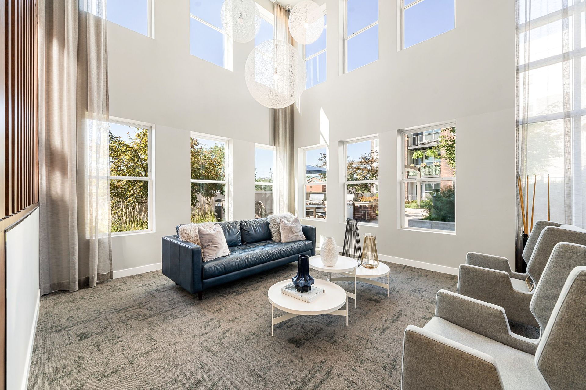 A bright living room with tall windows, blue sofa, and gray chairs.