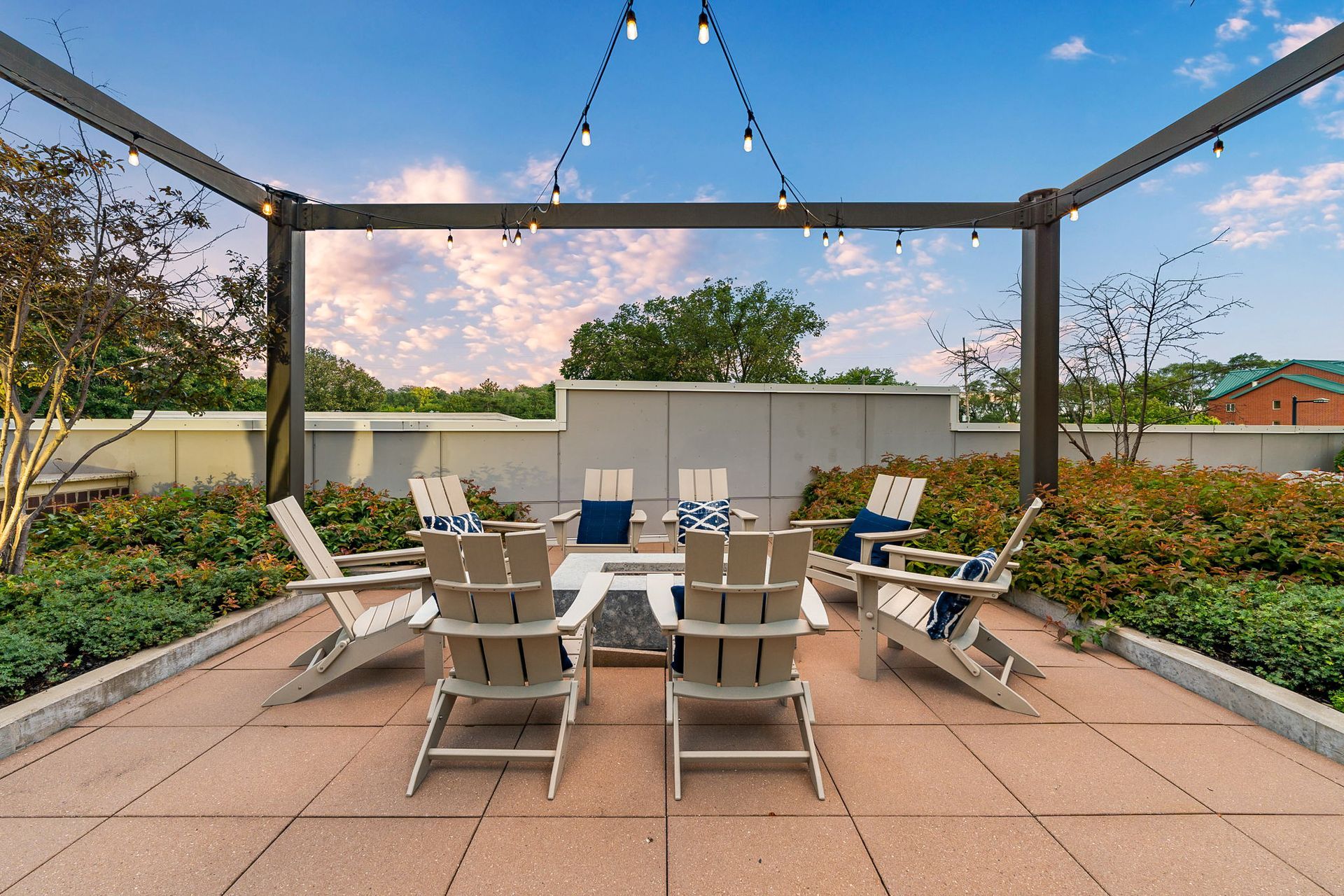 Outdoor patio with Adirondack chairs around a fire pit under string lights.