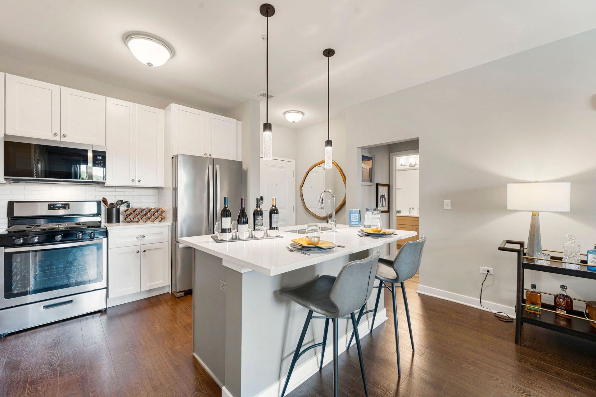 Modern kitchen with stainless steel appliances, white cabinets, gray island, and wooden floors.